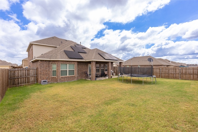 rear view of property with a trampoline, a yard, solar panels, and a patio