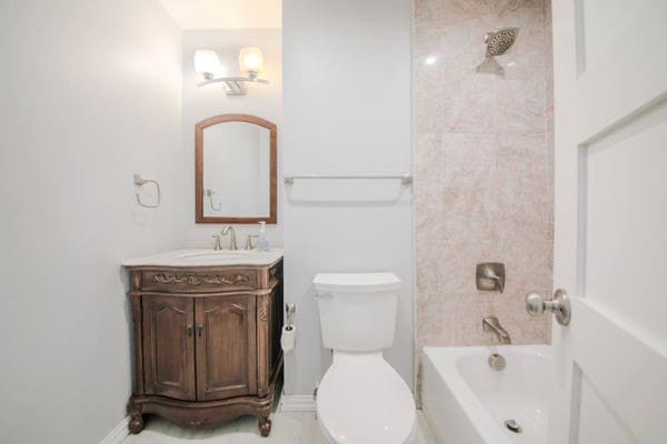 full bathroom featuring tiled shower / bath, vanity, and toilet