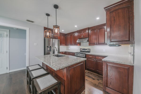 kitchen featuring a center island with sink, sink, dark wood-type flooring, and stainless steel appliances