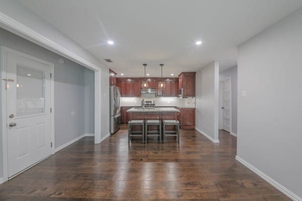 kitchen featuring an island with sink, dark hardwood / wood-style flooring, pendant lighting, stainless steel refrigerator, and a breakfast bar