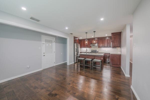 kitchen featuring hanging light fixtures, dark hardwood / wood-style flooring, a kitchen island, a kitchen bar, and stainless steel appliances