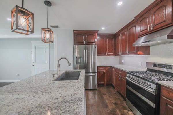 kitchen with hanging light fixtures, light stone counters, dark hardwood / wood-style flooring, sink, and stainless steel appliances