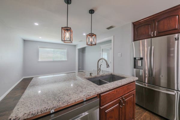 kitchen with sink, light stone countertops, stainless steel fridge with ice dispenser, pendant lighting, and dark hardwood / wood-style flooring