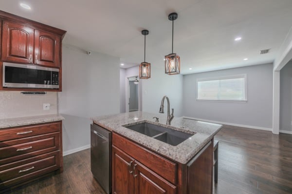 kitchen with an island with sink, dark hardwood / wood-style flooring, light stone countertops, sink, and stainless steel appliances