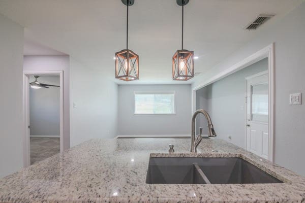 kitchen with ceiling fan, light stone countertops, sink, and hanging light fixtures