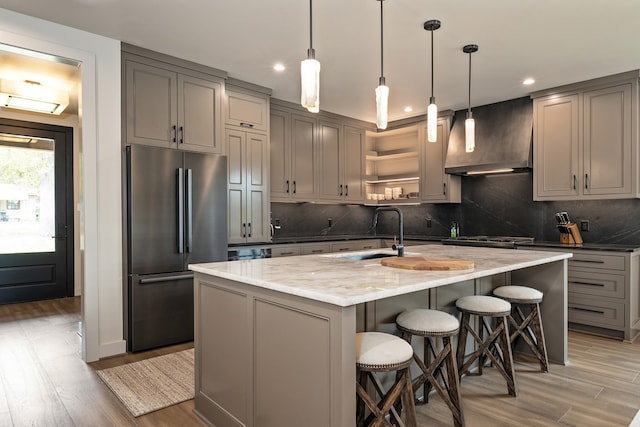 kitchen featuring light stone countertops, appliances with stainless steel finishes, light wood-type flooring, wall chimney exhaust hood, and hanging light fixtures