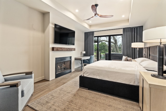 bedroom with access to exterior, a tray ceiling, light hardwood / wood-style flooring, and ceiling fan