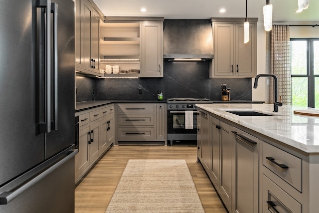 kitchen with gray cabinetry, high end appliances, wall chimney range hood, and sink