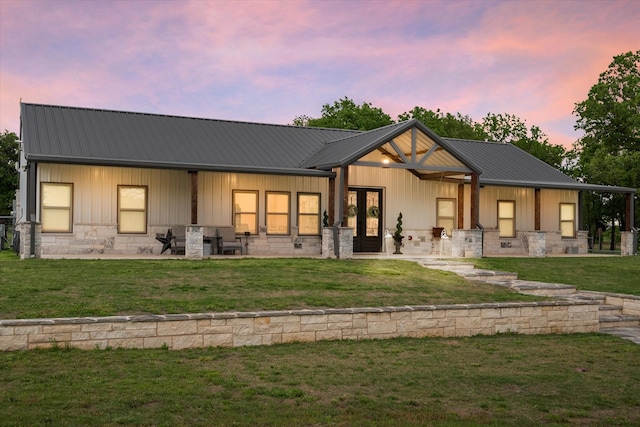 back of property at dusk with board and batten siding, a lawn, metal roof, stone siding, and a patio