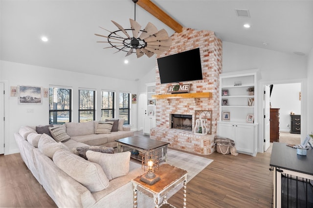 living room with ceiling fan, a fireplace, beam ceiling, hardwood / wood-style flooring, and high vaulted ceiling