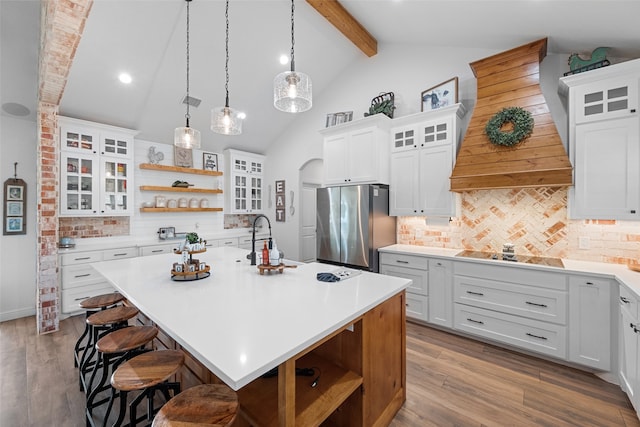 kitchen with backsplash, custom exhaust hood, stainless steel refrigerator, white cabinetry, and an island with sink