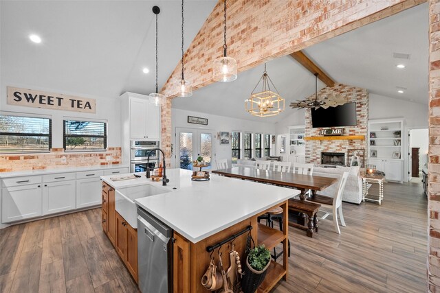 kitchen featuring white cabinets, a kitchen island with sink, appliances with stainless steel finishes, and a brick fireplace