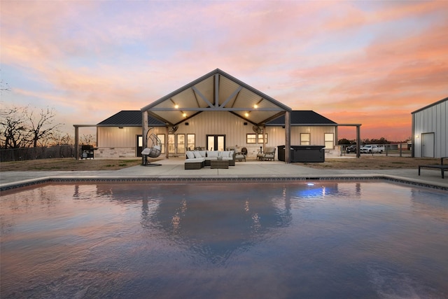 pool at dusk with a patio area, outdoor lounge area, and a hot tub