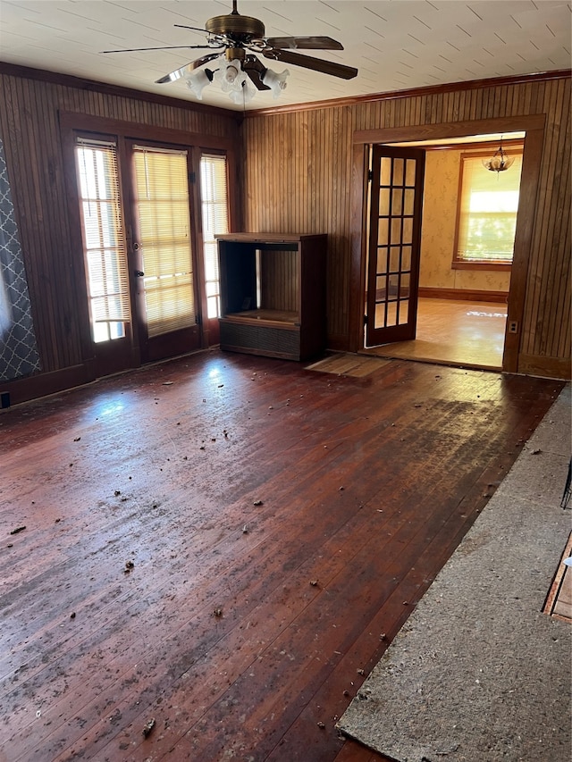 unfurnished living room featuring dark wood-type flooring, wood walls, ceiling fan, and ornamental molding