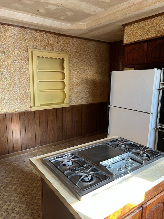 kitchen featuring a textured ceiling, stainless steel gas cooktop, white fridge, and wooden walls