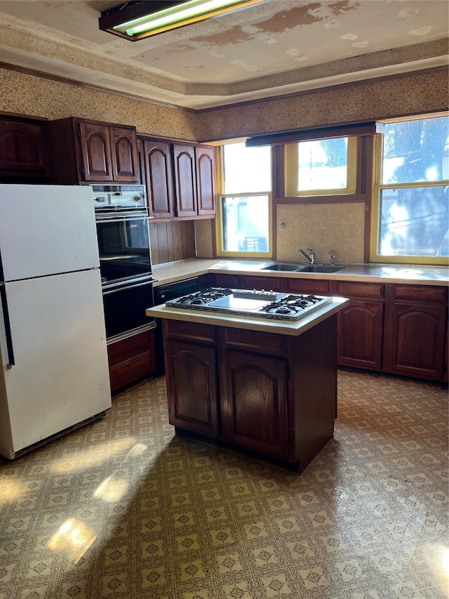 kitchen featuring stainless steel gas stovetop, sink, white fridge, a kitchen island, and ornamental molding