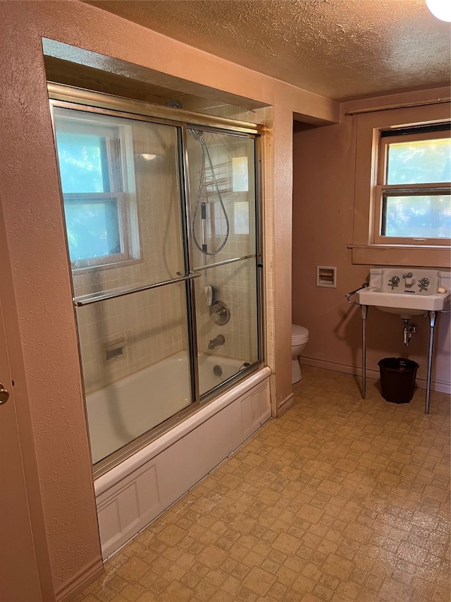 full bathroom featuring a textured ceiling, toilet, sink, and enclosed tub / shower combo