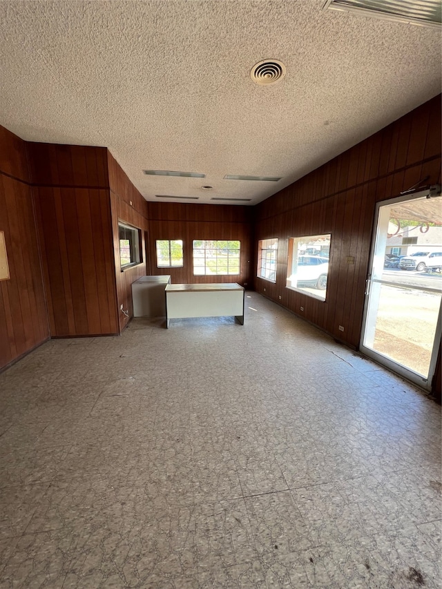 unfurnished living room featuring vaulted ceiling, wooden walls, and a textured ceiling