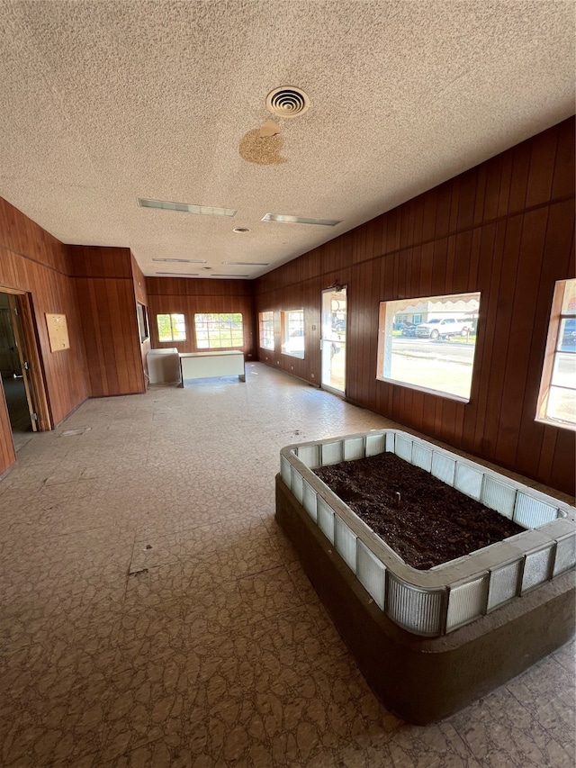 interior space with multiple windows, a textured ceiling, and wood walls