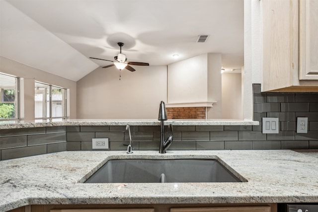 kitchen with vaulted ceiling, tasteful backsplash, light stone countertops, and sink