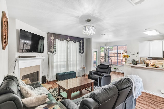 living room featuring a tile fireplace, an inviting chandelier, a textured ceiling, and light hardwood / wood-style flooring