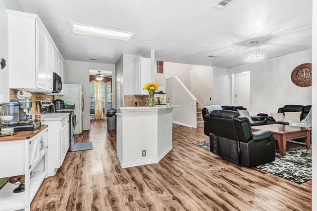 kitchen featuring stainless steel range with electric stovetop, ceiling fan with notable chandelier, light hardwood / wood-style flooring, decorative backsplash, and white cabinets