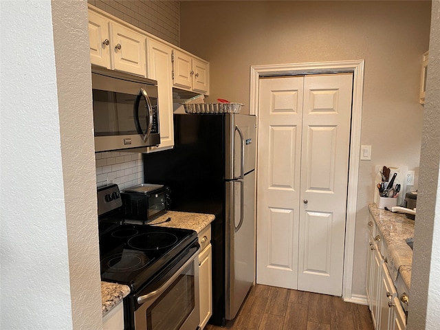 kitchen with white cabinetry, tasteful backsplash, stainless steel appliances, light stone countertops, and dark wood-type flooring