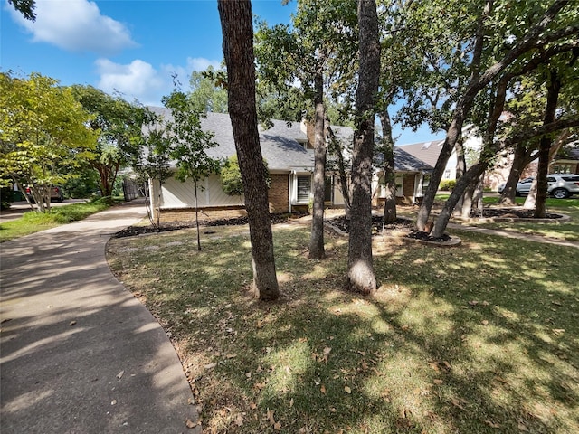 view of property hidden behind natural elements with driveway, an attached garage, a front lawn, and brick siding