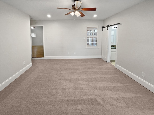 carpeted spare room with a barn door, baseboards, a ceiling fan, and recessed lighting