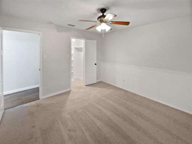 carpeted spare room featuring a textured ceiling, ceiling fan, wainscoting, and visible vents