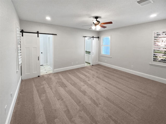 unfurnished bedroom with a barn door, baseboards, visible vents, a textured ceiling, and carpet flooring