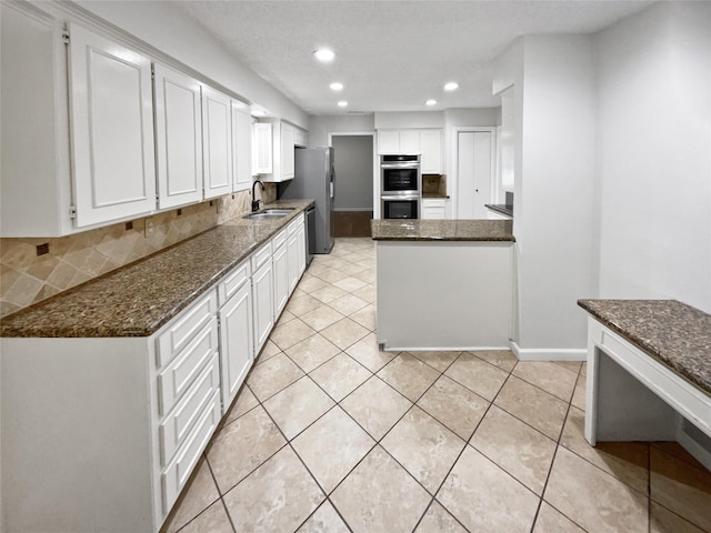 kitchen featuring tasteful backsplash, dark stone counters, stainless steel appliances, white cabinetry, and a sink