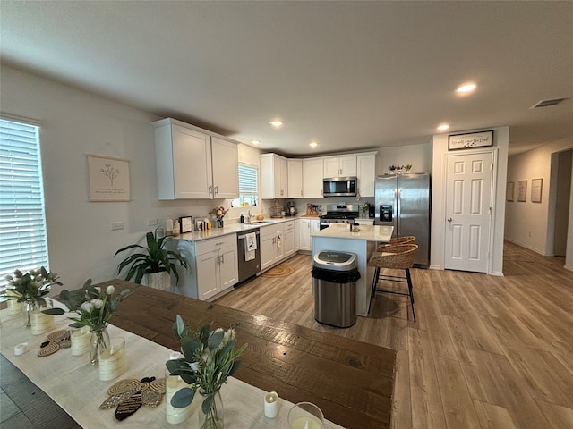 kitchen featuring white cabinets, a center island, light wood-type flooring, appliances with stainless steel finishes, and a breakfast bar area