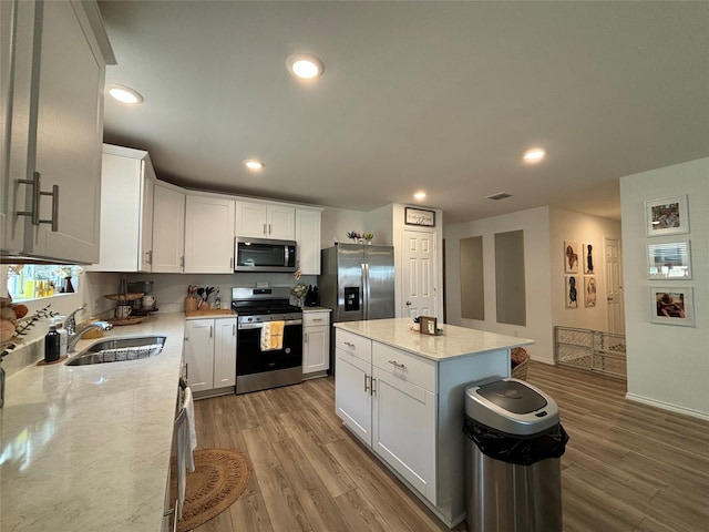 kitchen featuring white cabinetry, a kitchen island, light stone countertops, appliances with stainless steel finishes, and hardwood / wood-style flooring