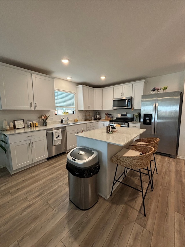 kitchen featuring a center island, hardwood / wood-style floors, appliances with stainless steel finishes, white cabinetry, and sink