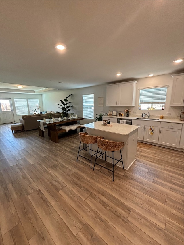 kitchen with a kitchen island, light hardwood / wood-style floors, stainless steel dishwasher, sink, and white cabinetry