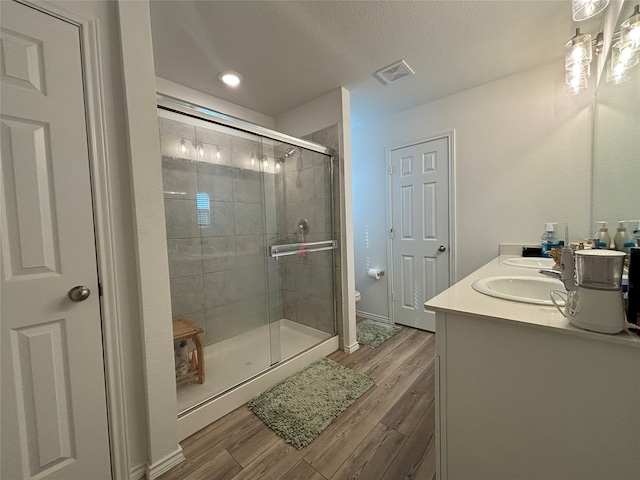 bathroom with a textured ceiling, vanity, walk in shower, toilet, and hardwood / wood-style flooring