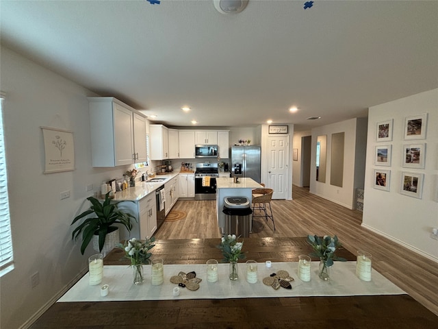 kitchen with white cabinets, appliances with stainless steel finishes, a kitchen island, and light hardwood / wood-style floors