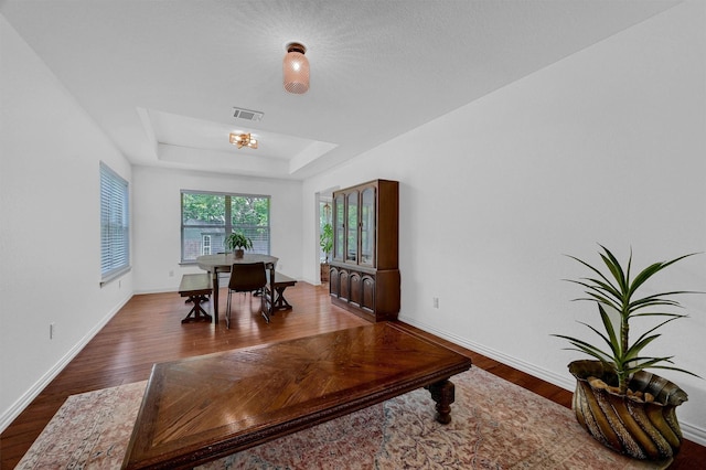 home office featuring a tray ceiling, visible vents, dark wood finished floors, and baseboards