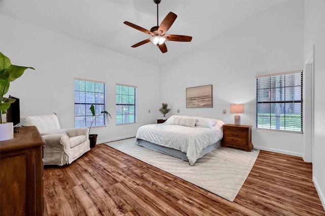 bedroom featuring baseboards, multiple windows, high vaulted ceiling, and wood finished floors