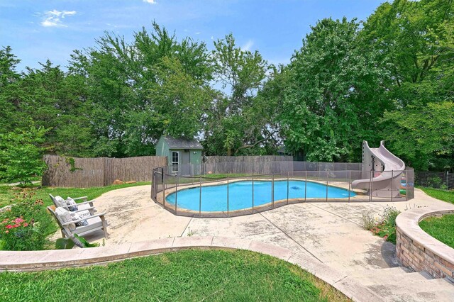 view of pool featuring a water slide, a patio, a lawn, and a storage unit