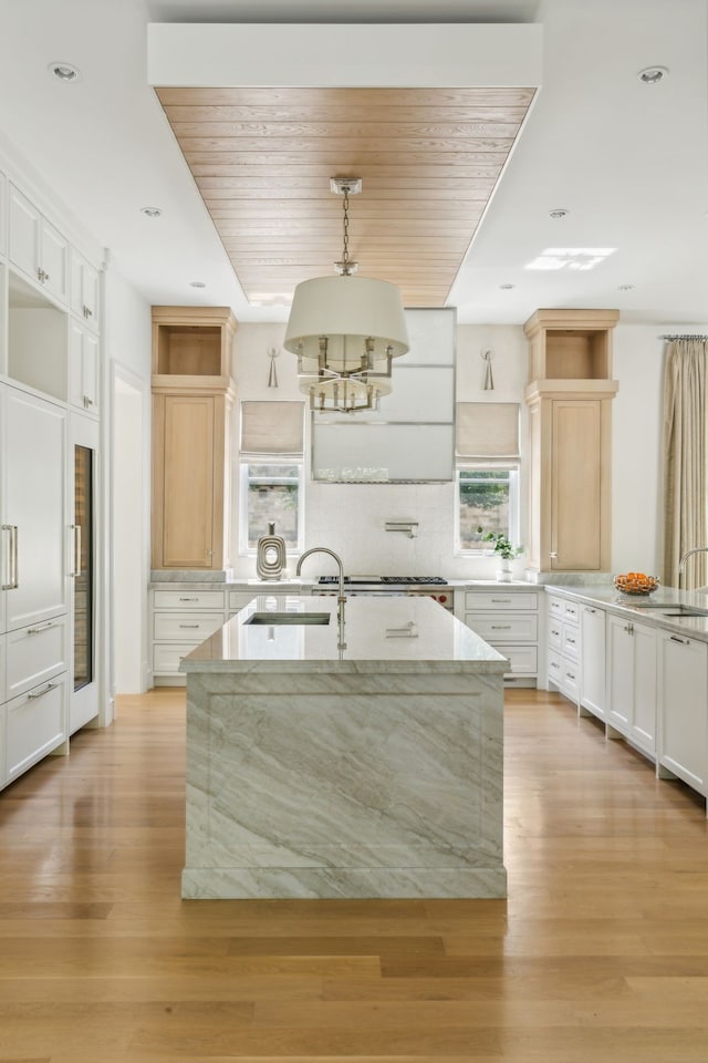 kitchen with a kitchen island with sink, light hardwood / wood-style floors, sink, light stone counters, and white cabinets