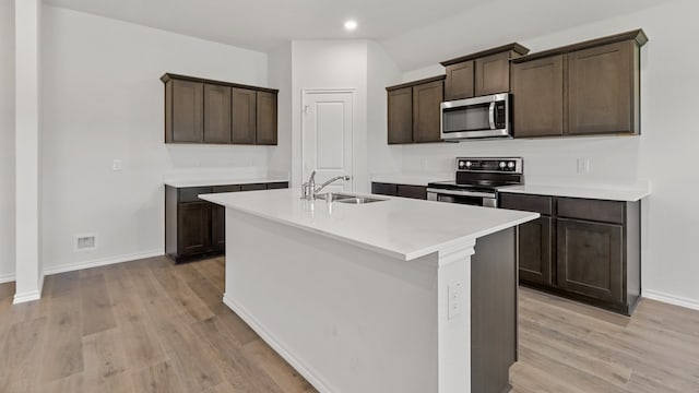 kitchen with stainless steel appliances, light wood-type flooring, dark brown cabinetry, a kitchen island with sink, and sink