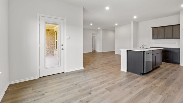 kitchen featuring light wood-type flooring, sink, an island with sink, dark brown cabinetry, and stainless steel dishwasher