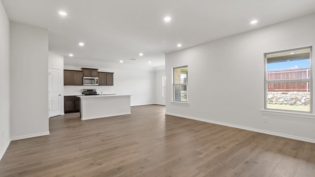 kitchen featuring a center island with sink, black range with electric cooktop, dark brown cabinets, and hardwood / wood-style flooring