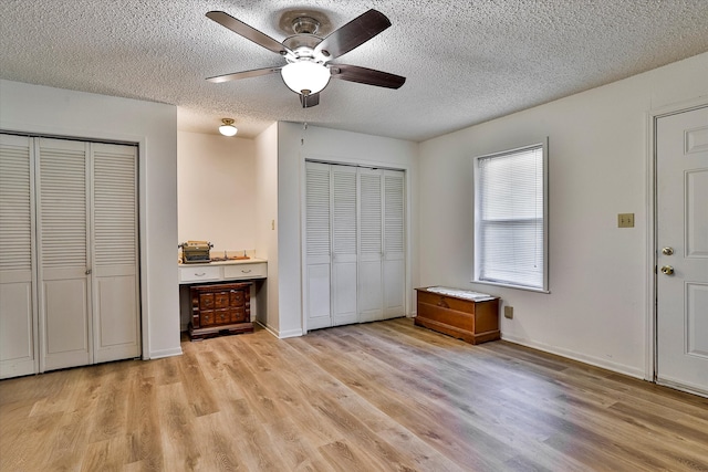 unfurnished bedroom featuring a textured ceiling, light hardwood / wood-style floors, ceiling fan, and multiple closets