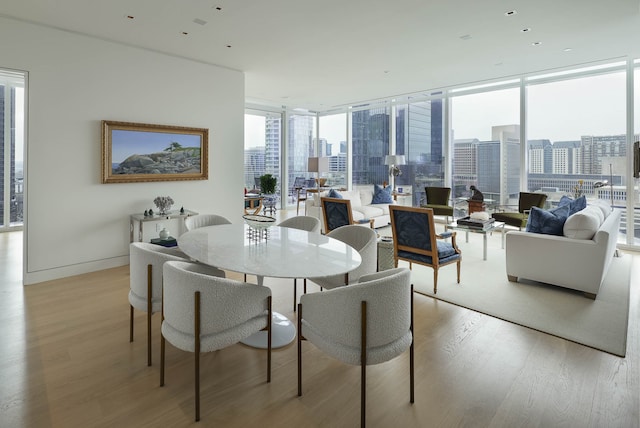 dining space with light wood-type flooring, a wall of windows, and a healthy amount of sunlight