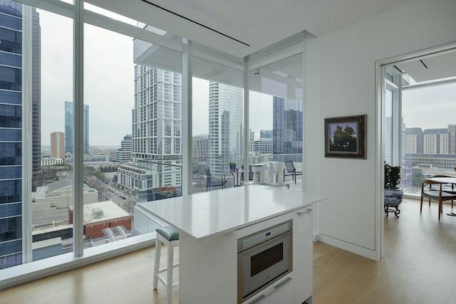 kitchen with stainless steel microwave, white cabinetry, light hardwood / wood-style flooring, and expansive windows