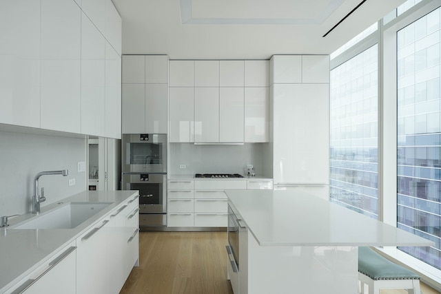 kitchen featuring white cabinets, a center island, stainless steel double oven, light hardwood / wood-style floors, and sink