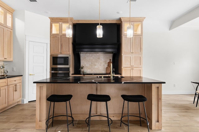 kitchen with light hardwood / wood-style flooring, appliances with stainless steel finishes, sink, an island with sink, and pendant lighting